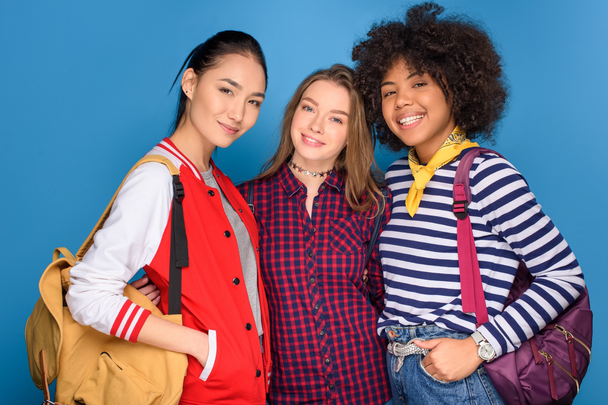 female multicultural students posing with backpacks, isolated on blue